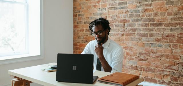 a man sitting at a table in front of a laptop by Microsoft 365 courtesy of Unsplash.